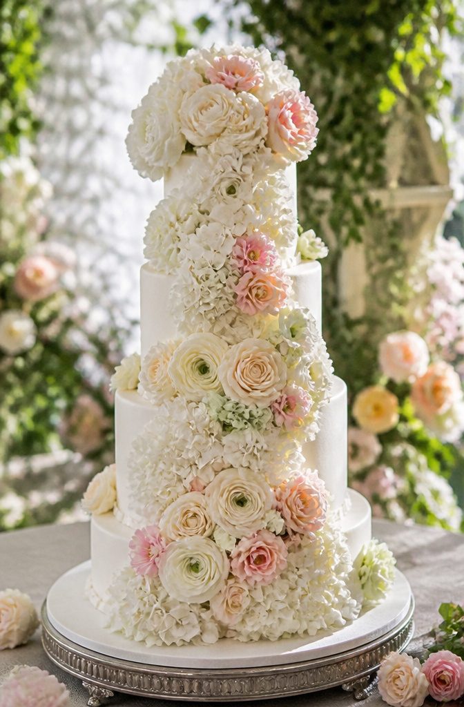 Elegant White Wedding Cake Recipe 13 Cake covered in colorful flowers in a garden setting.